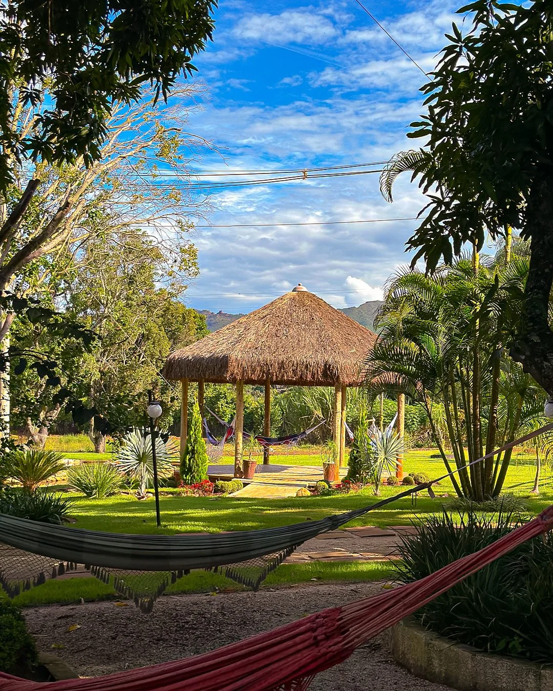 Quiosque com redes em meio ao gramado e jardim